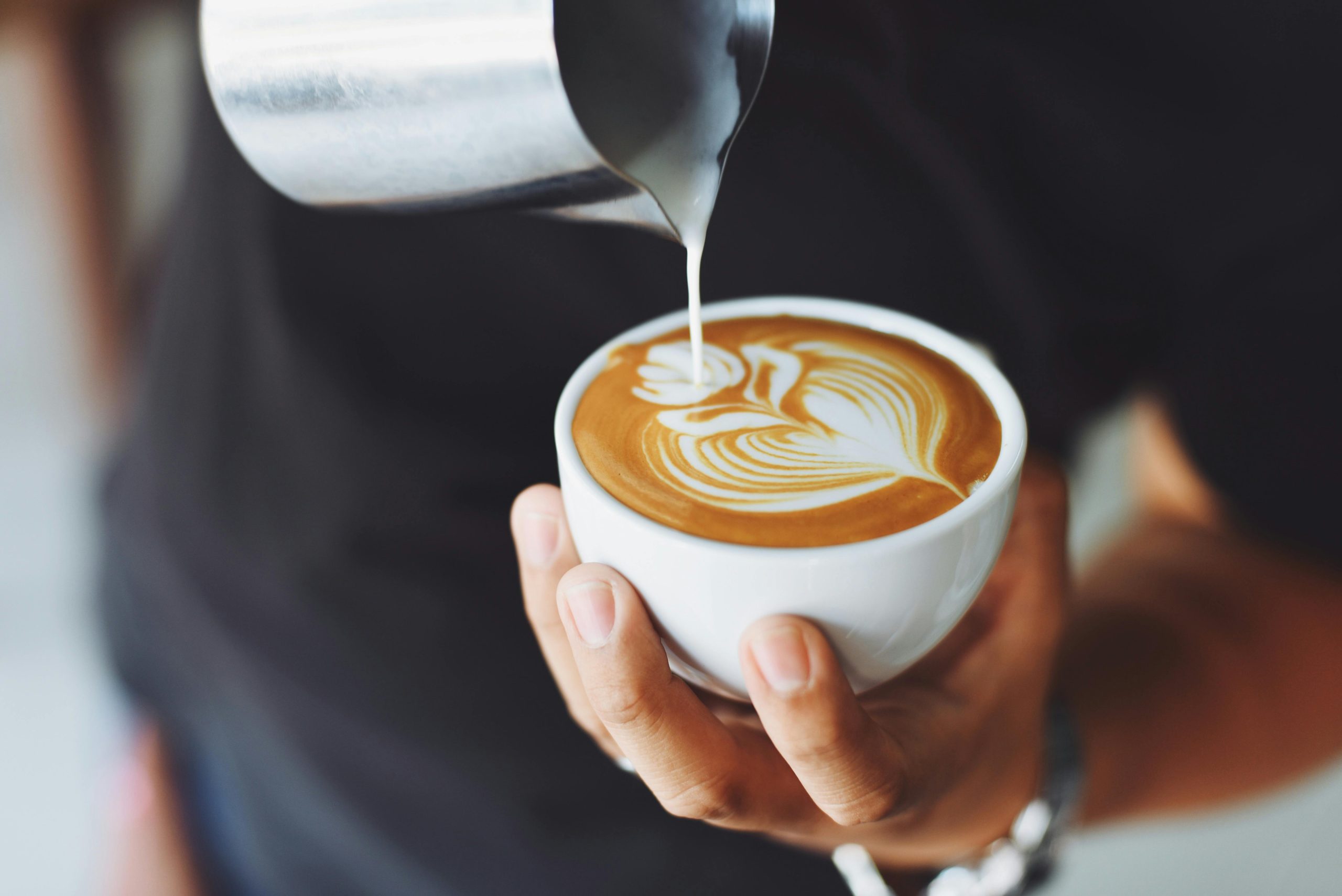 A person pouring milk into a cup of coffee